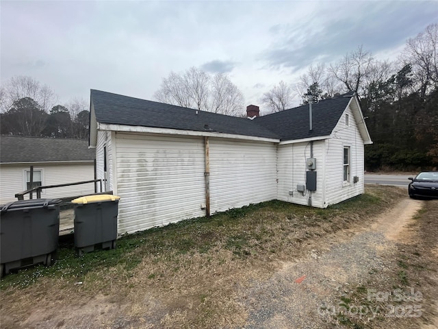 view of side of home with roof with shingles and a chimney