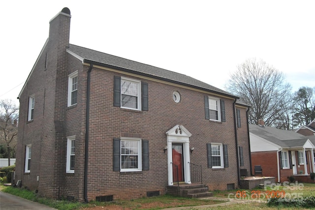 colonial inspired home featuring brick siding and a chimney