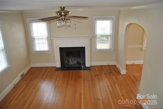 unfurnished living room featuring a fireplace with flush hearth, arched walkways, crown molding, and hardwood / wood-style floors