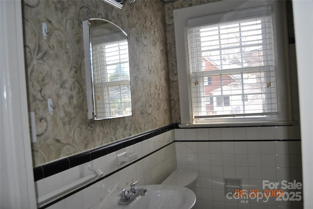 bathroom featuring a wealth of natural light, wainscoting, a sink, and wallpapered walls