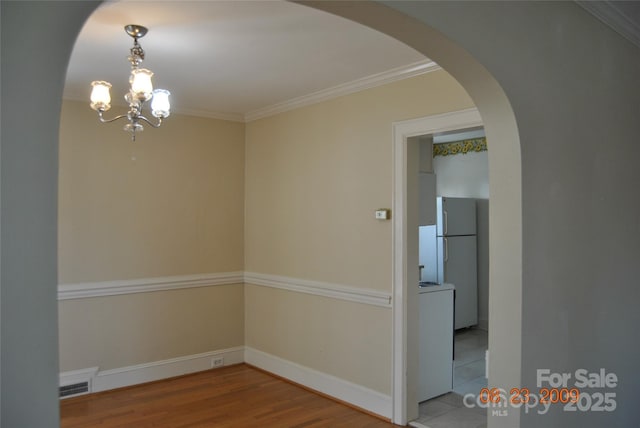 spare room featuring visible vents, arched walkways, wood finished floors, and ornamental molding