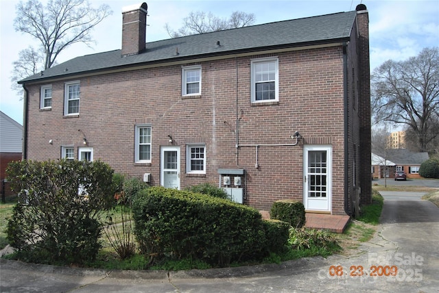 rear view of house featuring brick siding and a chimney