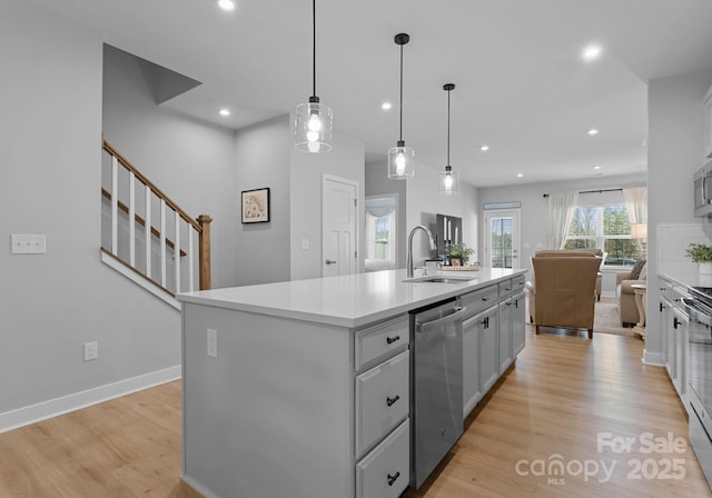 kitchen with open floor plan, appliances with stainless steel finishes, a sink, and light wood-style flooring