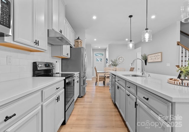 kitchen featuring stainless steel appliances, light countertops, a sink, and under cabinet range hood