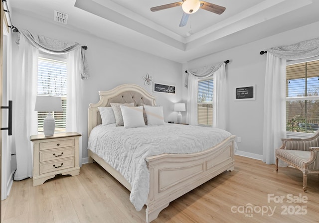 bedroom featuring a tray ceiling, multiple windows, light wood-type flooring, and visible vents