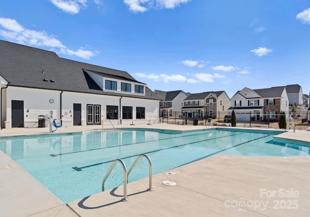 pool with a patio area, fence, and a residential view