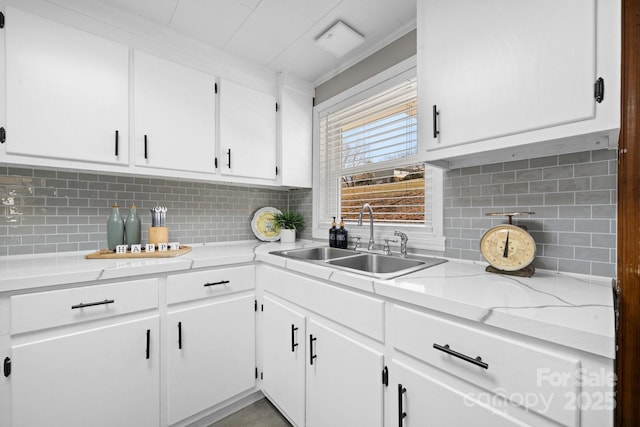 kitchen featuring tasteful backsplash, white cabinets, light countertops, and a sink