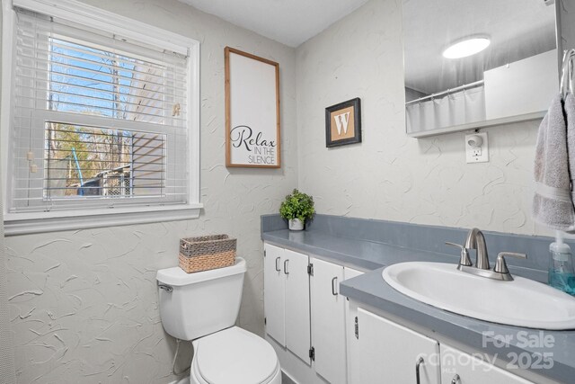 bathroom featuring toilet, a textured wall, and vanity