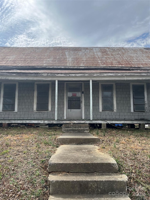 entrance to property with a shingled roof and a porch