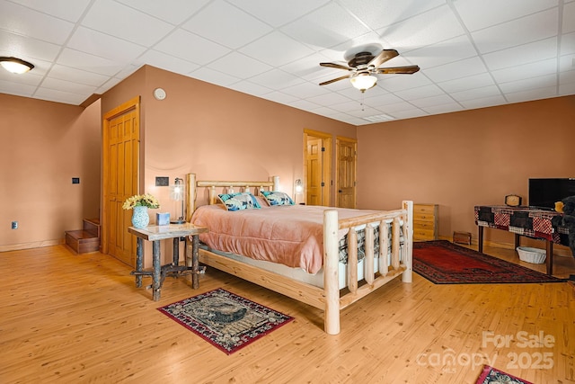 bedroom with a drop ceiling, ceiling fan, baseboards, and wood finished floors