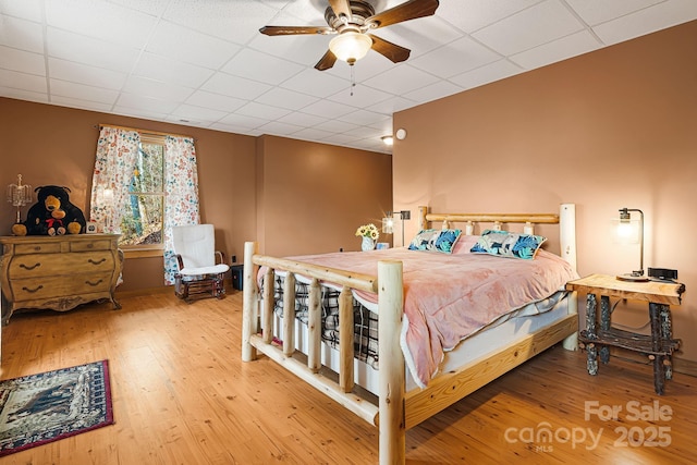 bedroom with ceiling fan, a drop ceiling, and wood finished floors