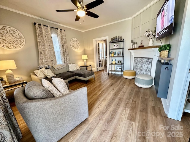 living room featuring a fireplace, wood finished floors, a ceiling fan, baseboards, and ornamental molding