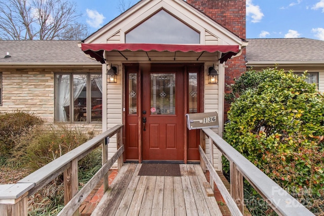 doorway to property featuring stone siding and roof with shingles