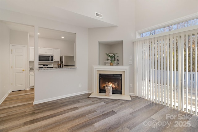 unfurnished living room with visible vents, a lit fireplace, light wood-style flooring, and baseboards