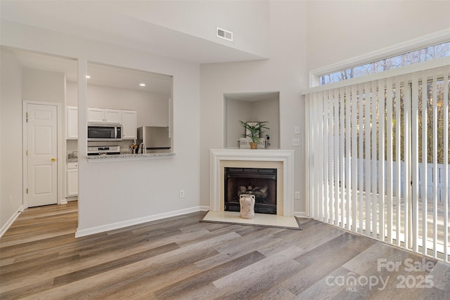 unfurnished living room with a fireplace with raised hearth, visible vents, baseboards, and wood finished floors