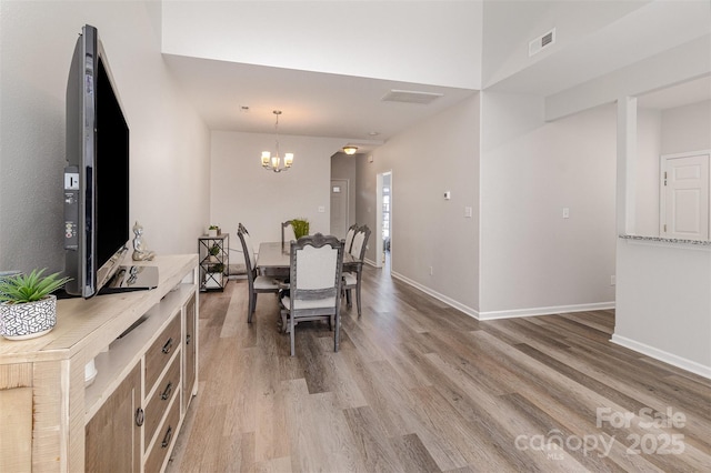 dining space featuring baseboards, light wood-type flooring, visible vents, and a notable chandelier