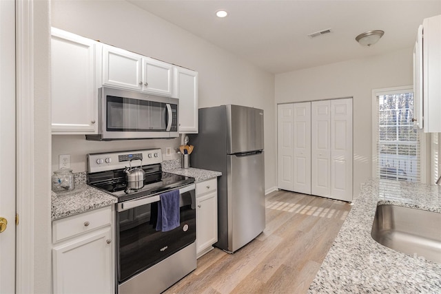 kitchen with visible vents, white cabinets, light stone counters, stainless steel appliances, and light wood-type flooring