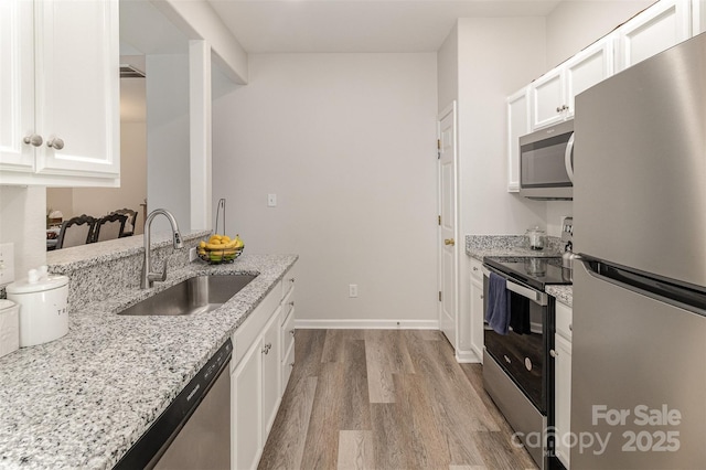 kitchen featuring light stone counters, stainless steel appliances, a sink, white cabinets, and light wood-type flooring