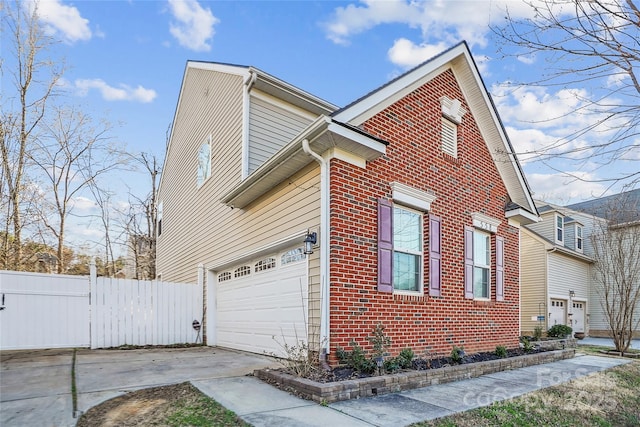 view of property exterior featuring driveway, a garage, fence, and brick siding