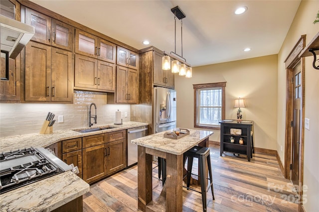 kitchen featuring a sink, appliances with stainless steel finishes, decorative backsplash, light stone countertops, and light wood finished floors