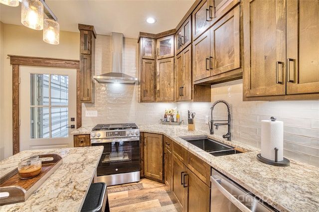 kitchen with decorative backsplash, brown cabinets, stainless steel appliances, wall chimney range hood, and a sink