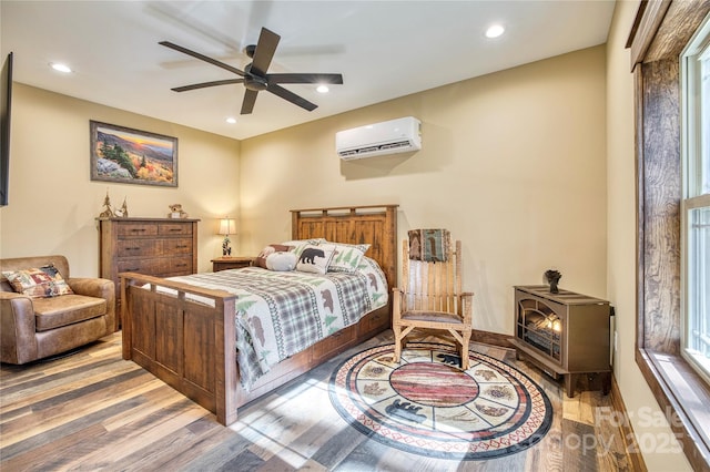 bedroom with a wood stove, recessed lighting, wood finished floors, and a wall mounted air conditioner