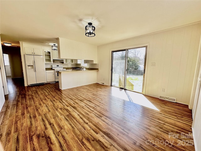 kitchen with a peninsula, white refrigerator with ice dispenser, visible vents, gas stove, and dark wood finished floors