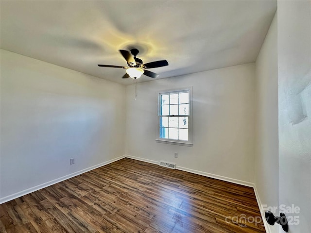 spare room with dark wood-style floors, a ceiling fan, visible vents, and baseboards