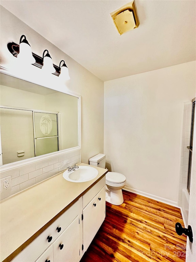 bathroom featuring baseboards, decorative backsplash, toilet, wood finished floors, and vanity