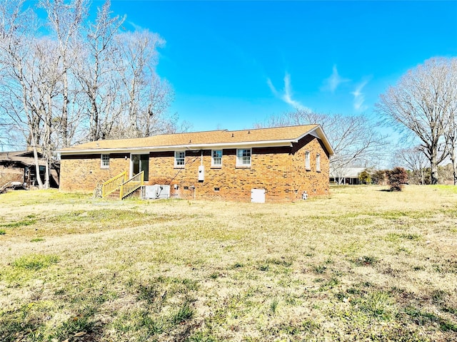 rear view of property featuring entry steps, a lawn, and brick siding