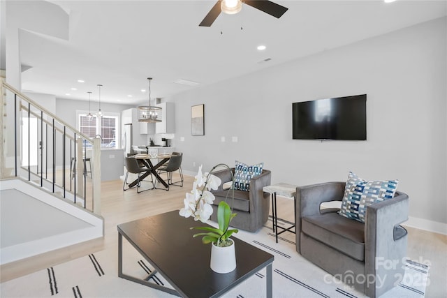 living area featuring light wood finished floors, stairs, ceiling fan with notable chandelier, and recessed lighting