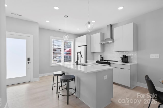 kitchen featuring a breakfast bar, a sink, wall chimney range hood, tasteful backsplash, and a center island with sink