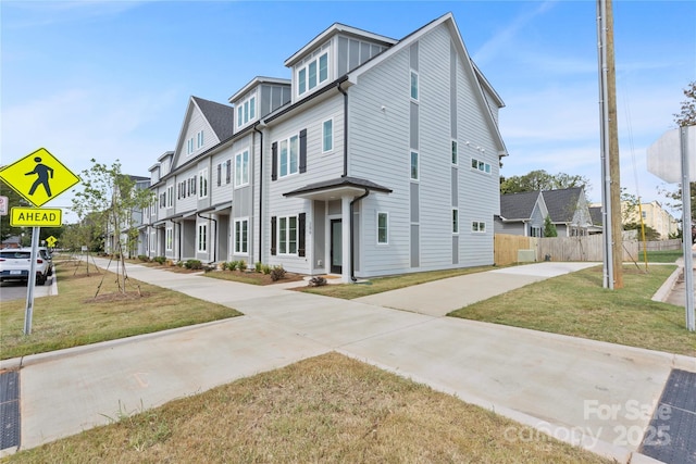 view of front facade featuring a residential view, fence, and a front lawn