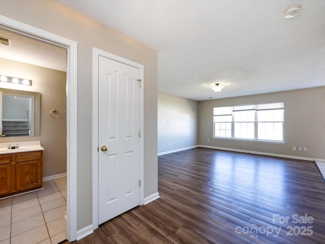 interior space with visible vents, light wood-style flooring, a sink, a textured ceiling, and baseboards