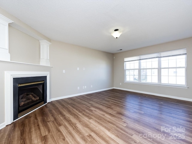 unfurnished living room with a textured ceiling, wood finished floors, visible vents, baseboards, and a glass covered fireplace