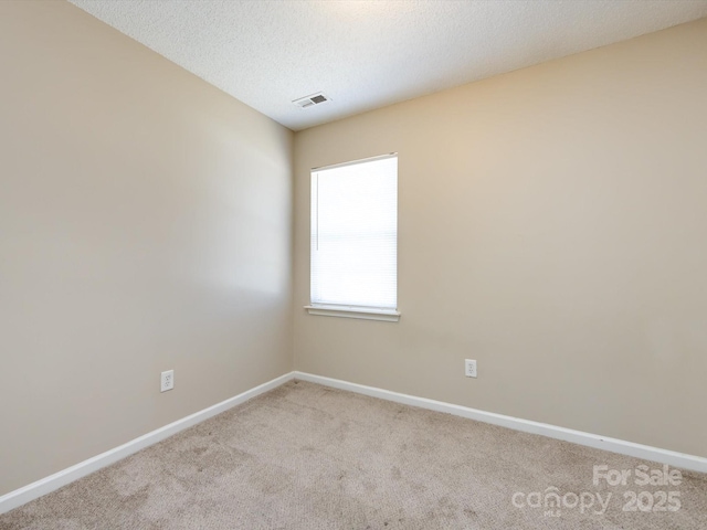 spare room featuring visible vents, light carpet, baseboards, and a textured ceiling
