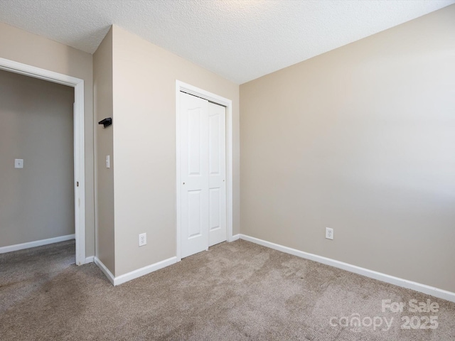 unfurnished bedroom featuring carpet, a closet, a textured ceiling, and baseboards