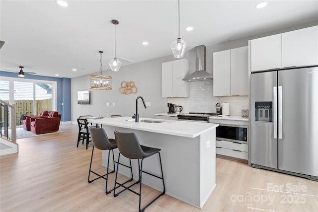 kitchen with a kitchen island with sink, stainless steel appliances, a sink, wall chimney exhaust hood, and tasteful backsplash