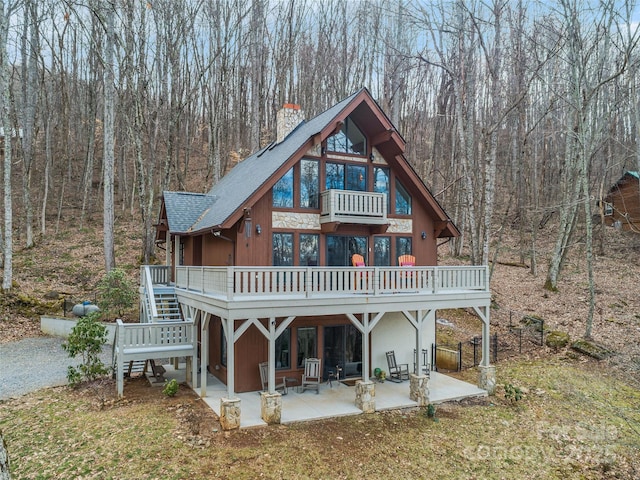 back of house with roof with shingles, a patio, a view of trees, a balcony, and a wooden deck