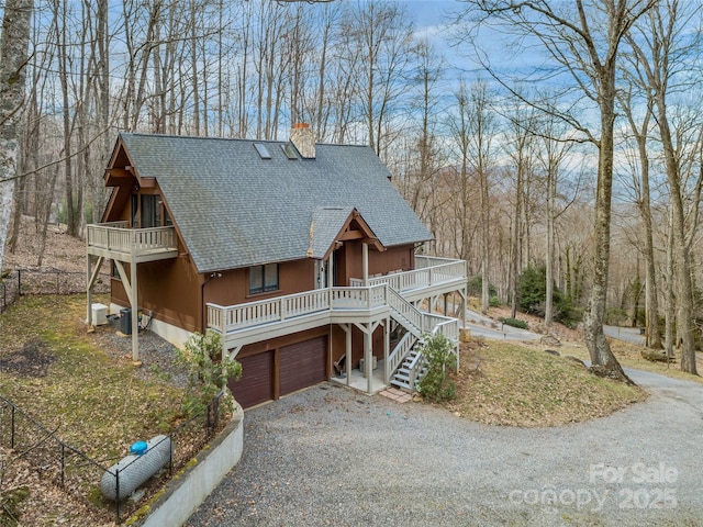 view of front of house featuring driveway, a garage, a chimney, stairway, and roof with shingles