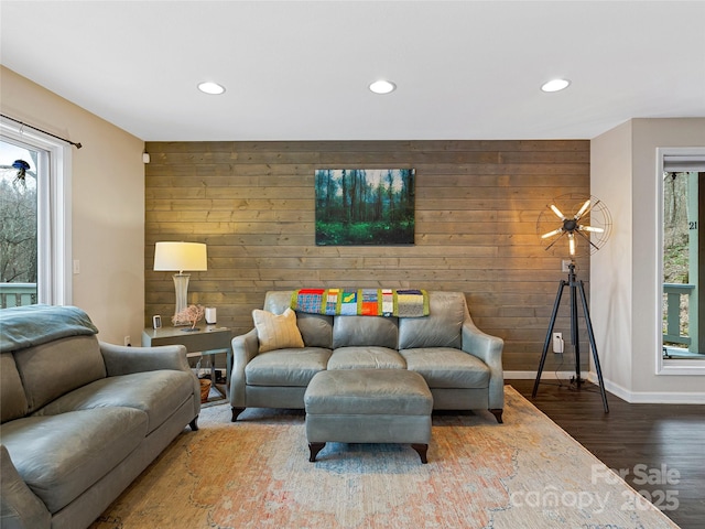 living area featuring wooden walls, baseboards, an accent wall, wood finished floors, and recessed lighting