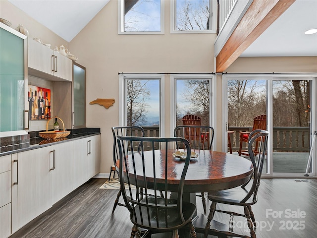 dining room featuring dark wood-type flooring, wet bar, plenty of natural light, and high vaulted ceiling