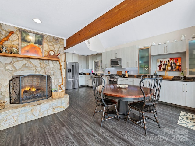 dining room with a stone fireplace, dark wood finished floors, beam ceiling, and recessed lighting