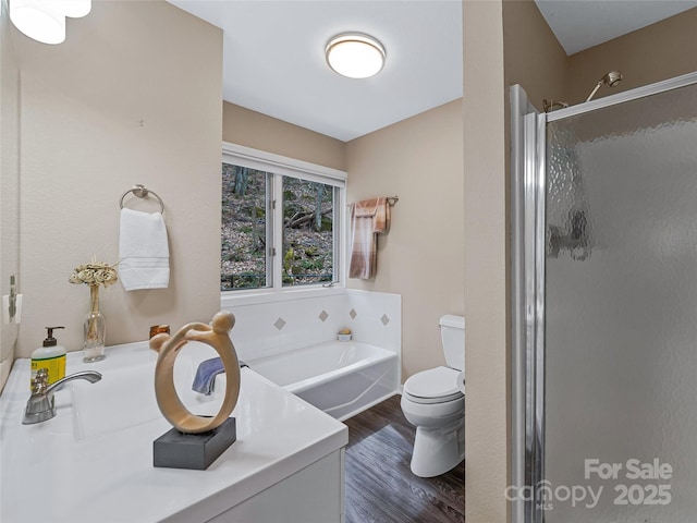 bathroom featuring a garden tub, a shower stall, toilet, and wood finished floors