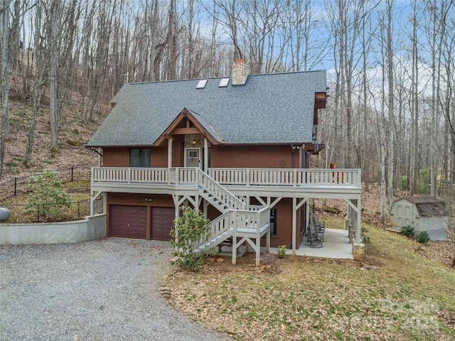 rustic home featuring gravel driveway, a chimney, a shingled roof, a garage, and stairs