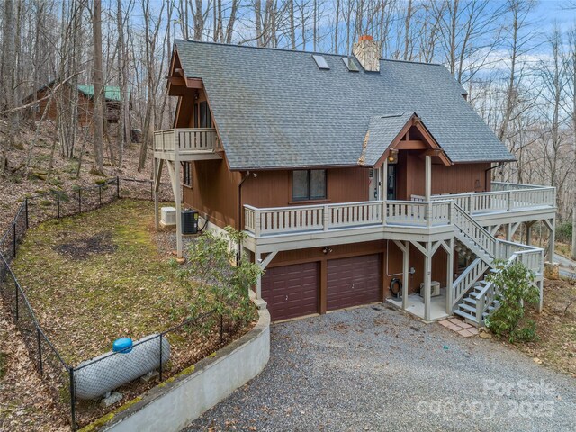 rustic home with driveway, a chimney, roof with shingles, stairs, and central AC