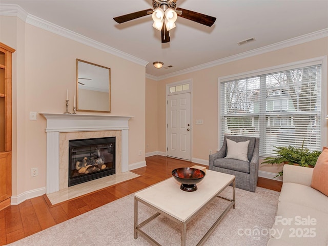 living room with a premium fireplace, wood finished floors, visible vents, baseboards, and ornamental molding