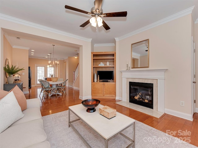 living area with baseboards, ornamental molding, wood finished floors, built in shelves, and a high end fireplace