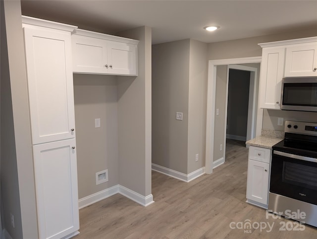 kitchen featuring light wood finished floors, baseboards, white cabinetry, and stainless steel appliances