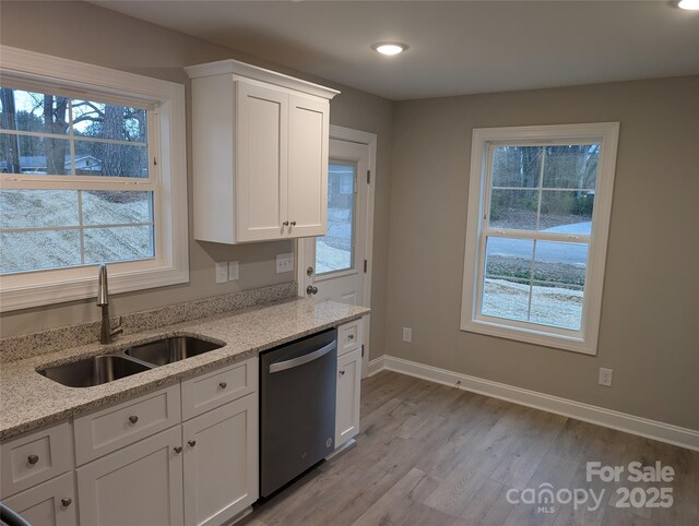 kitchen featuring light wood finished floors, baseboards, stainless steel dishwasher, white cabinetry, and a sink